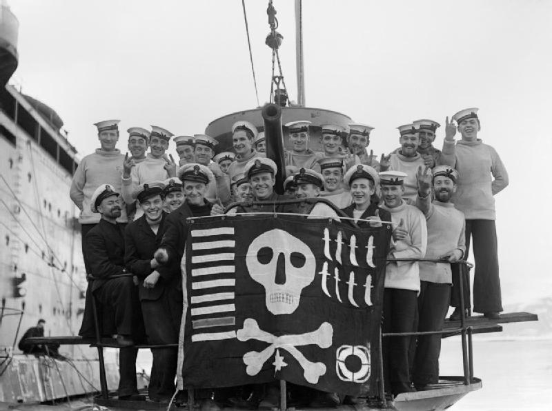Members of the crew of HMS Utmost with their "Jolly Roger" success flag, photographed alongside HMS Forth in Holy Loch, on their return from a year's service in the Mediterranean, 6 February 1942. (via Wikipedia)